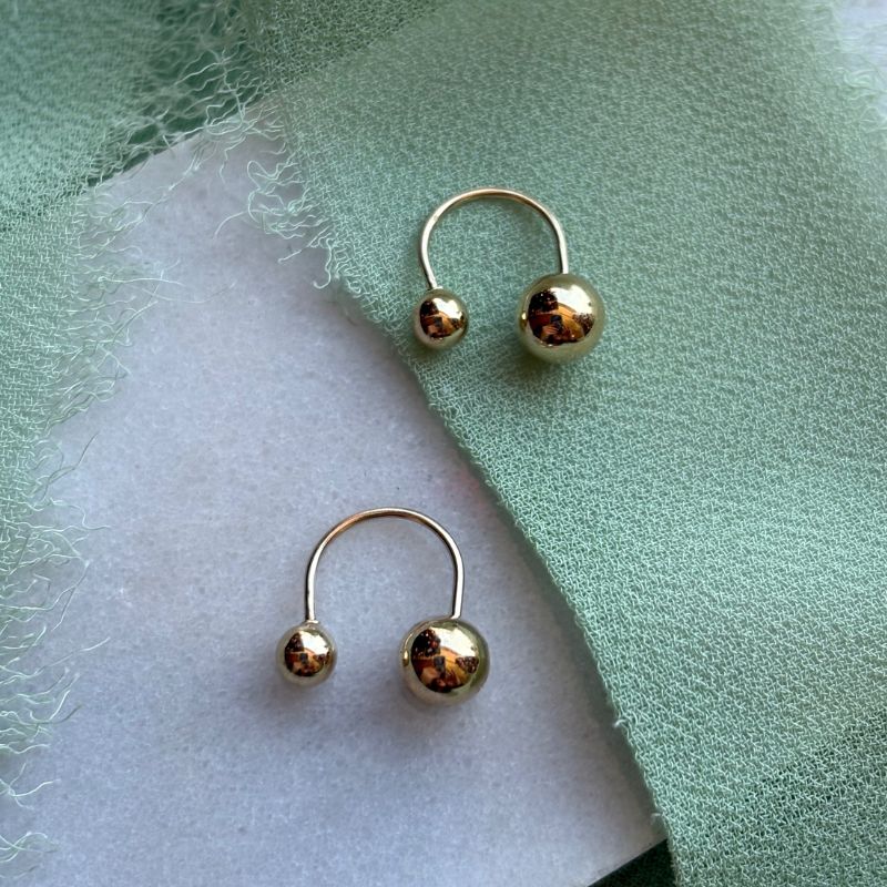 Alma 14kt yellow gold studs shown on a white marble tray with green linen draped around