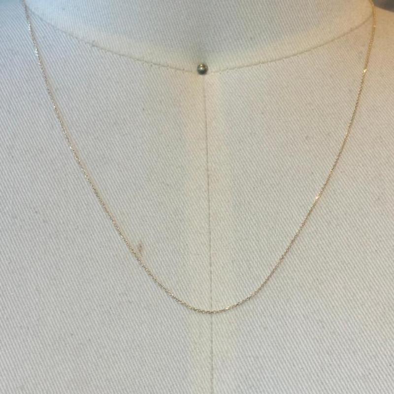 This beautiful and dainty 14 kt solid yellow gold chain is shown on an off white cream bust.