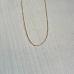 This beautiful and dainty 14 kt solid yellow gold chain is shown on a wooden background.