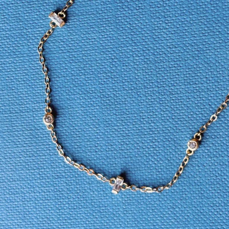 Yellow gold chain bracelet with bezet set and half bezel set crystals shown on blue book background.