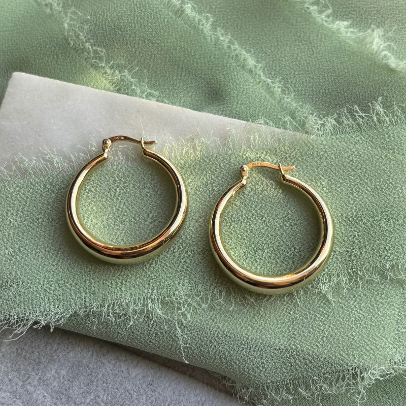 A pair of 14kt yellow gold hoops on a marble tray with green linen.