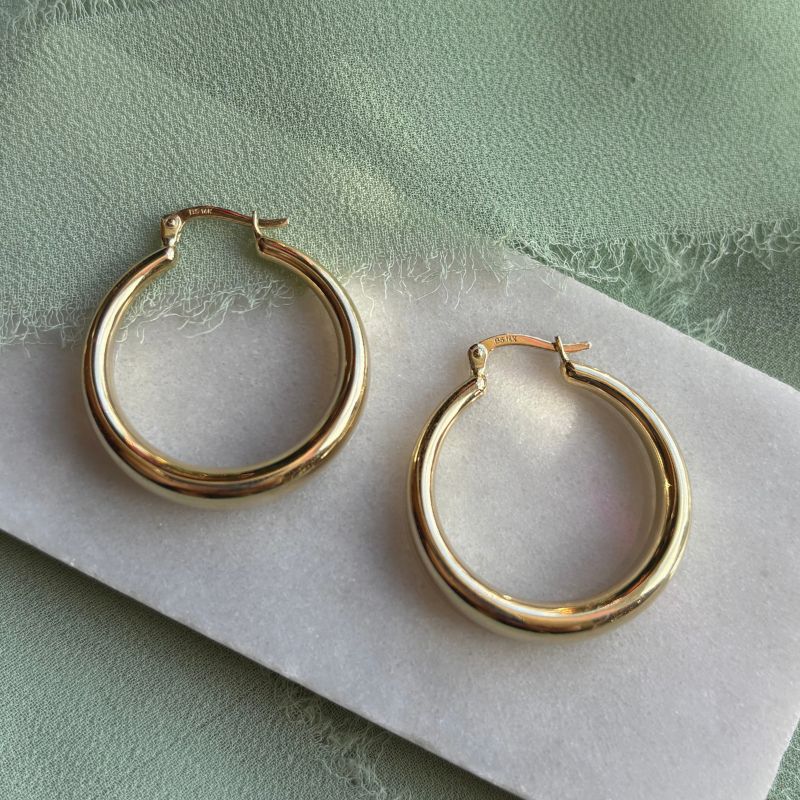 
                  
                    Load image into Gallery viewer, A pair of 14kt yellow gold hoops on a marble tray with green linen.
                  
                