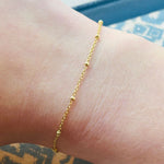 Shown on a right wrist, a yellow gold bracelet with small balls spaced evenly.