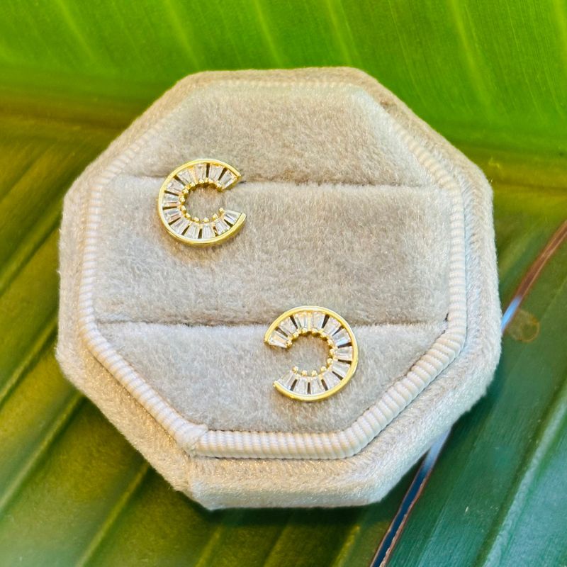 Yellow gold semi circle studs with tapered baguettes on a display tray with a green background.