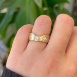 Notched cigar band with diamonds modeled on left ring finger with green background.