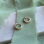 A pair of 14kt yellow gold huggies displayed on a marble tray with green ribbon