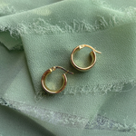 SIde view of a pair of 14 kt yellow gold hoops on a green linen tray.