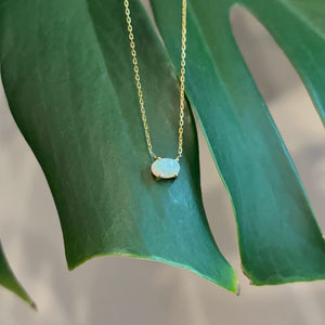 
                  
                    Load image into Gallery viewer, A single oval opal set with rounded prongs on a dazzling diamond cut 14kt yellow gold chain shown in front of a green leaf.
                  
                