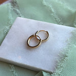 A pair of 14kt yellow gold huggies styled on a marble tray with light green linen draped around