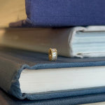 14kt and baguette rondel placed upright on stack of blue and white books.