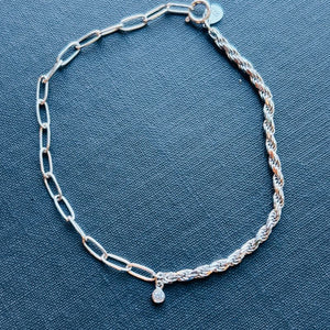 
                  
                    Load image into Gallery viewer, Half paperclip and half rope bracelet joined in the middle by a bezel set round crystal shown on a blue book
                  
                