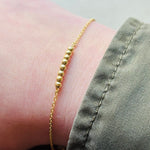 Yellow gold beaded bracelet modeled on right wrist with a green jacket