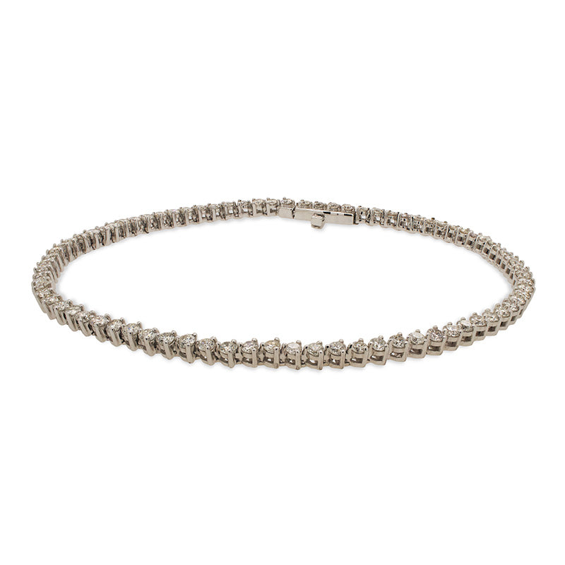 A classic diamond tennis bracelet cast in 14 kt white gold with a box clasp on a white background.