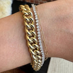 A large gold curb chain, round tennis bracelet cast in white gold and dainty, gold paperclip bracelet on the wearer's wrist for scale.