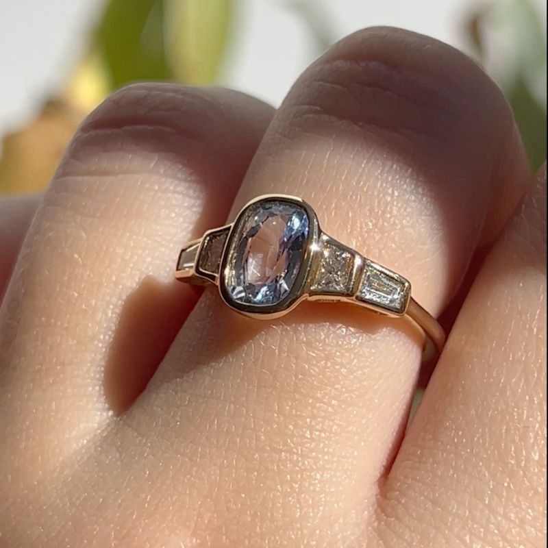 
                  
                    Load image into Gallery viewer, Cast in 14 kt gold, this light blue oval sapphire center stone is flanked by four trapezoid and baguette cut and diamonds. This bezel set ring is low profile and is perfect as an engagement ring.
                  
                